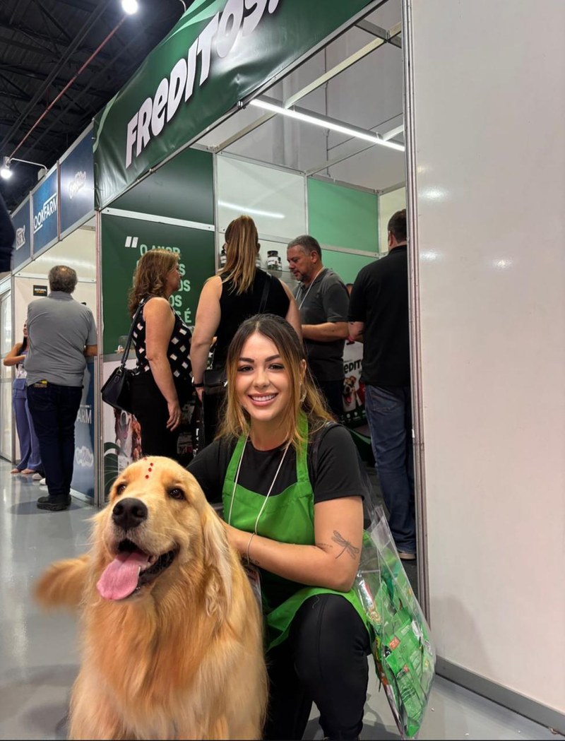 Promotora da HAVC em ação de troca de brindes em estande de feira, com cão golden retriever